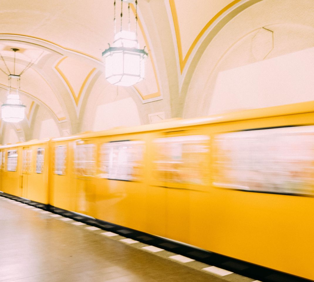 Bildbeschreibung: Eine gelbe Berliner U-Bahn fährt durch einen hell erleuchteten U-Bahnhof und ist nur verschwommen zu sehen. 
