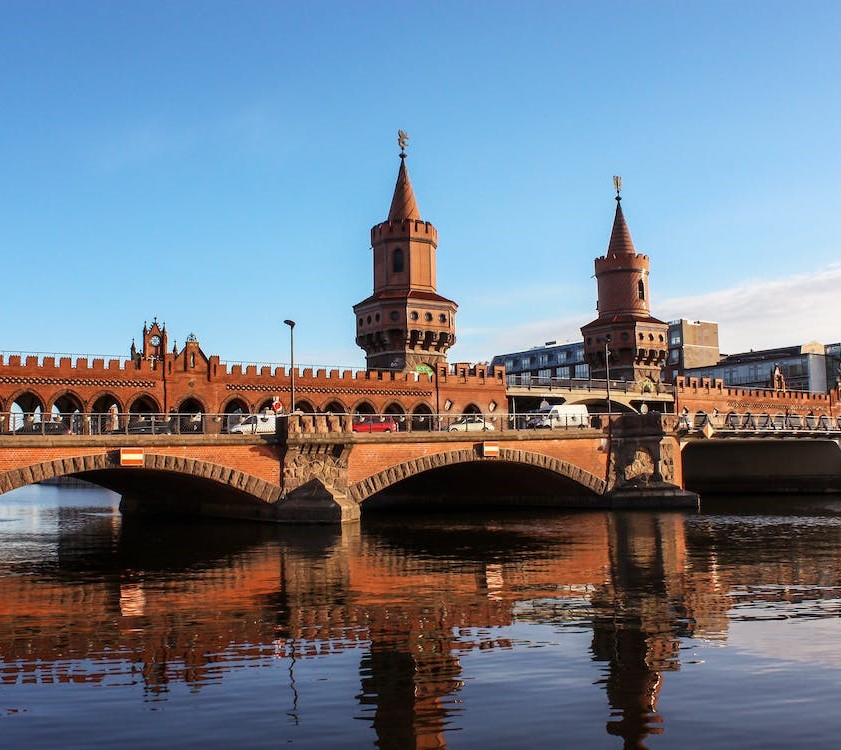 Bildbeschreibung: Die Oberbaumbrücke in Berlin Friedrichshain. Der Himmel ist blau und die Brücke spiegelt sich in der Spree. 